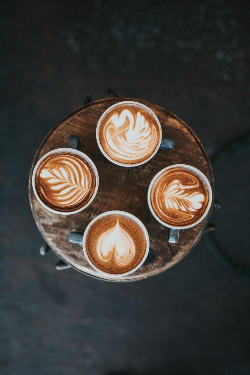 An image of a barista carefully pouring hot water over a pour-over coffee dripper placed on a wooden table, with a scenic NL cafe background.