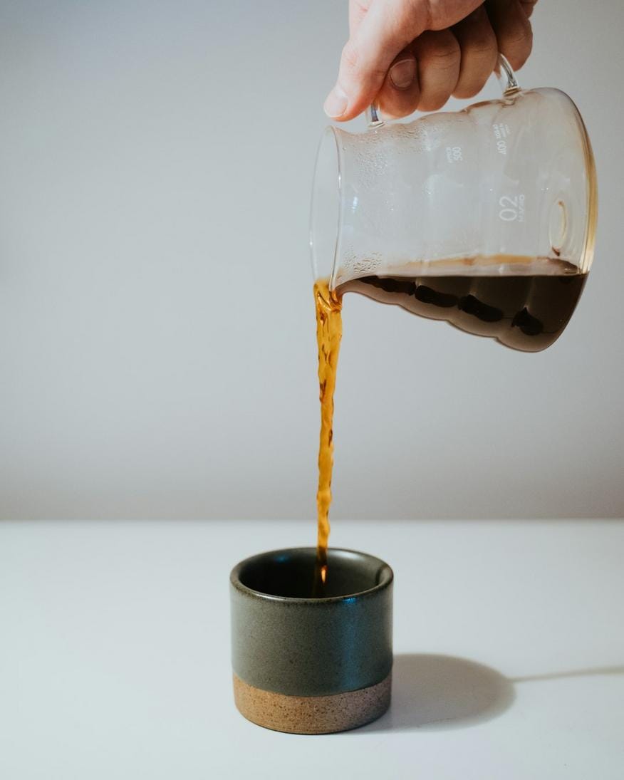 Close-up of a barista pouring hot water over a pour-over coffee cone with beans and kettle